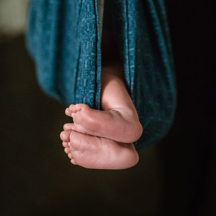 Baby feet visible peeking out from a blue patterned weighing sling.